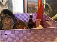 Purple woven basket filled with various decorative plates, bottles, and decanters.
