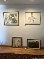 Four framed art prints on wall and floor showing various subjects including classical figures, horse rider, abstract face, and field scene
