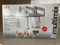 Braun Multimix 3-in-1 system box showing hand mixer with attachments for mixing, blending, and chopping. Multi-language text highlights the 3 functions and power of 220 watts.