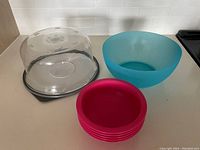 Plastic cake container with clear lid and black base, large blue bowl, and four small pink bowls