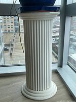 White painted fluted column with vertical fluting, standing by a window, shown with plant pots on top