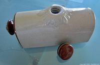 Side view of tan and brown salt glazed loaf-shaped stoneware foot warmer with open top and ceramic stopper next to it.