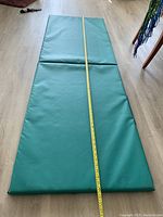 Green folding foam exercise mat laid flat on the floor with tape measure showing approximately 6 feet length.