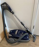 Kenmore Progressive True HEPA canister vacuum cleaner with attached hose, metal extension wand, and floor nozzle attachment, placed on wooden floor by wall.