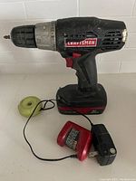 Rechargeable Craftsman 19.2V cordless drill with attached battery and red charger base lying on a flat surface against a white tiled wall.