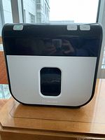 Front view of the compact paper shredder, black and white color with control buttons on top and a viewing window on the front waste bin.