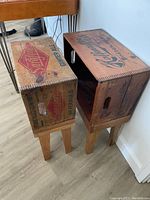 Pair of vintage wooden box side tables with manufacturer markings visible, standing beside a chair on a wood floor.