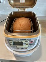 Opened bread maker showing freshly baked loaf inside baking pan.
