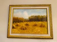 Full view of the painting showing the field with haystacks, trees in the background, and decorative gold frame.