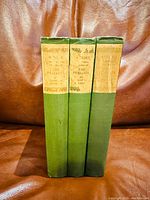 Three hardcover books with green cloth spines and paper title labels, standing vertically on a brown leather surface.