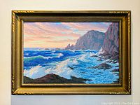 Full view of painting in gold-tone frame showing sunset over rocky coastline and crashing waves