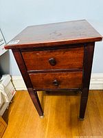 Front view showing two drawers with round wooden knobs, rectangular top, and legs with repairs.