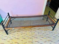 Folded bed frame showing the full structure laid out on floor, featuring metal mesh and wooden side frame with stamped branding.