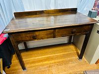 Full front view of antique oak writing desk with two drawers and raised back edge on top.