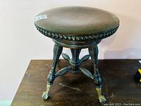 Front view of the antique height adjustable wood piano stool with turned legs and cast iron feet with glass balls.