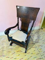 Front-right angle view of the antique walnut rocking chair showing large wooden back panel, armrests, and upholstered seat with wear.