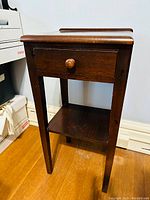 Front view photo showing the walnut side table with one drawer and lower shelf, four tapered legs, and the backsplash on top.