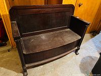 Front angled view of dark stained oak bench, curved back, closed hinged seat and turned legs