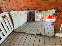 Full view of large rectangular mirror leaning against brick wall on porch flooring