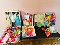 Three open cases with dolls and piles of clothes