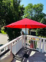 Red outdoor umbrella open, showing canopy and pole on a patio deck with green trees in background.