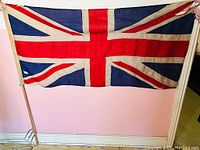 Full view of vintage Union Jack flag held horizontally showing the red, white, and blue cross design and beige border.