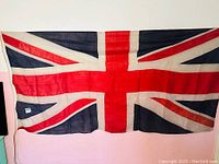 Full view of the vintage Union Jack flag hanging showing entire flag design and condition.