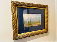 Angled view of the framed chalk pastel landscape showing the decorative gold frame and navy matting.