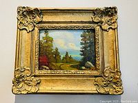 Frontal image of the ornate gold-framed oil painting on board depicting a landscape scene with trees and sky.