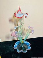 Front-right angle view of victorian art glass epergne showing three pink trumpet-shaped flowers with ruffled edges and a blue ruffled base