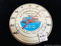 Front view of round 12-inch advertising thermometer/barometer showing printed image of old truck and company text.