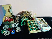 Wide view showing all ornaments including two wooden nativity scenes, blue-green glass baubles in box, star-shaped floral ornaments, figurines, and green tree candles.
