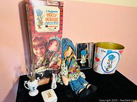 Photo showing the boxed Holly Hobbie cloth doll, small mirror, china pieces, and tin litho garbage can all together on table.