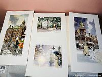 Three vintage William Biddle prints laid out on a table showing different urban scenes, all unframed.