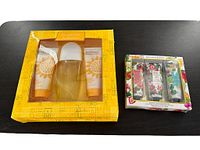 Both gift sets on a black surface, showing packaging and contents through window: Elizabeth Arden yellow box and Orchard and Vine floral box.
