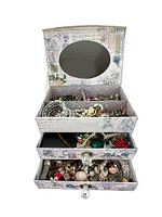 Full view of open decorative jewelry box showing mirror and three drawers filled with costume jewelry pieces.