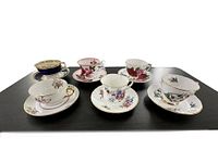 Overview of six vintage bone china tea cup and saucer sets arranged on black surface.