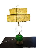 Front view of the lamp showing green glass base, brass elements, and two-tier fiberglass lampshade with black squiggle pattern on yellow
