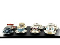 Eight assorted vintage cup and saucer sets arranged in one row displaying variety of colors and patterns.