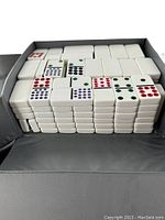 Open case showing stacked white domino tiles with multiple colored pips arranged in rows.