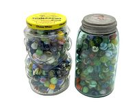 Two vintage jars filled with a variety of colorful vintage and antique marbles, one a Mario Brothers Cheez Whiz jar with a yellow lid and the other a Ball Mason jar with a metal lid.