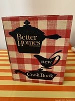 Front cover of 1960's Better Homes and Gardens New Cookbook with red and white checkered pattern and black kitchenware silhouettes.