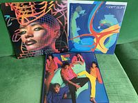 Three vinyl LP records including Grace Jones, Robert Plant, and The Rolling Stones lying on a green surface, showing front covers.