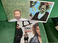 Three LP records displayed showing cover art for Iron & Wine, Joe Walsh, and INXS.