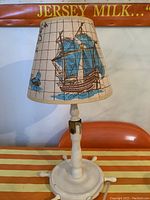Front view showing sailboat on the lampshade, white wooden ship wheel base, and adjustable joint for positioning lamp.