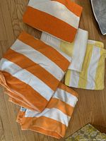 Five bath towels with orange and yellow stripes on a wooden floor.