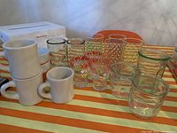 Full view of all glassware and mugs displayed on orange and cream striped tablecloth.