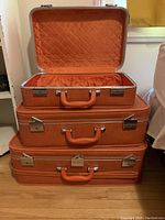 Stack of three vintage orange soft-sided suitcases, largest with lid open showing the orange quilted interior