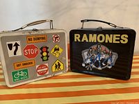 Front view of the two tin lunchboxes, one with 1970s road sign designs and one with Ramones band artwork.