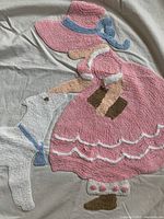 Close-up of chenille applique depicting a girl in a pink dress and bonnet with a white lamb, showing detailed texture and colors.